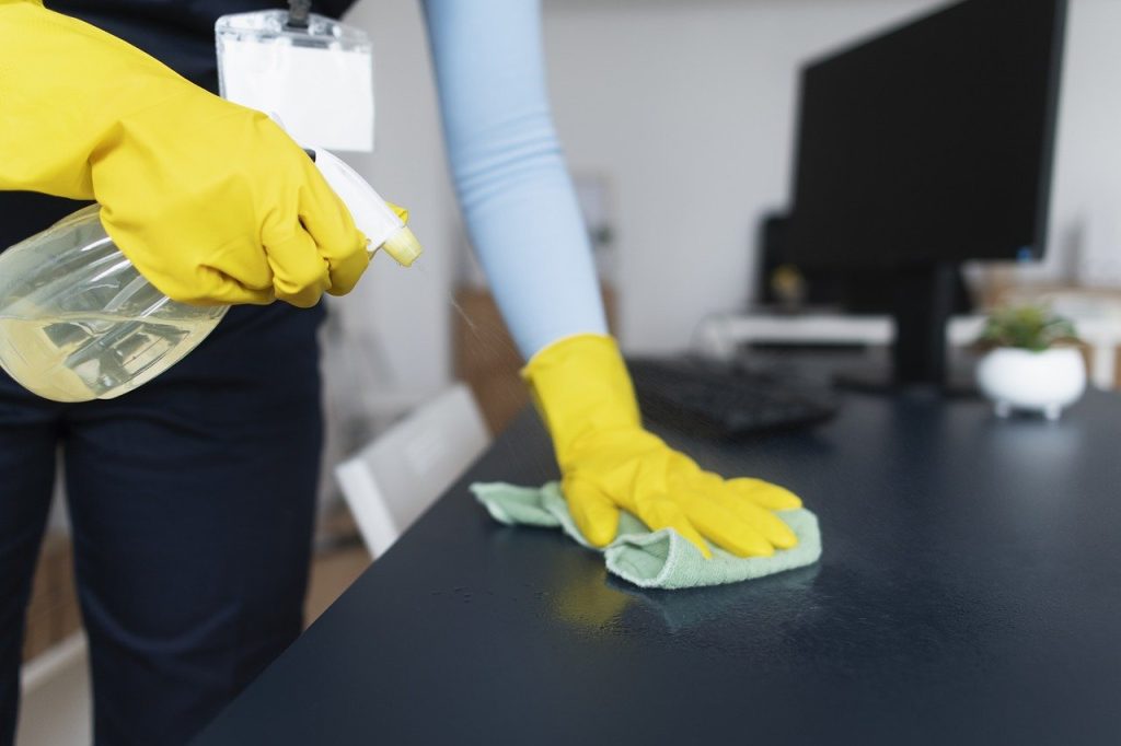 A lady cleaning a surface with gloves, rags and disinfecting spray